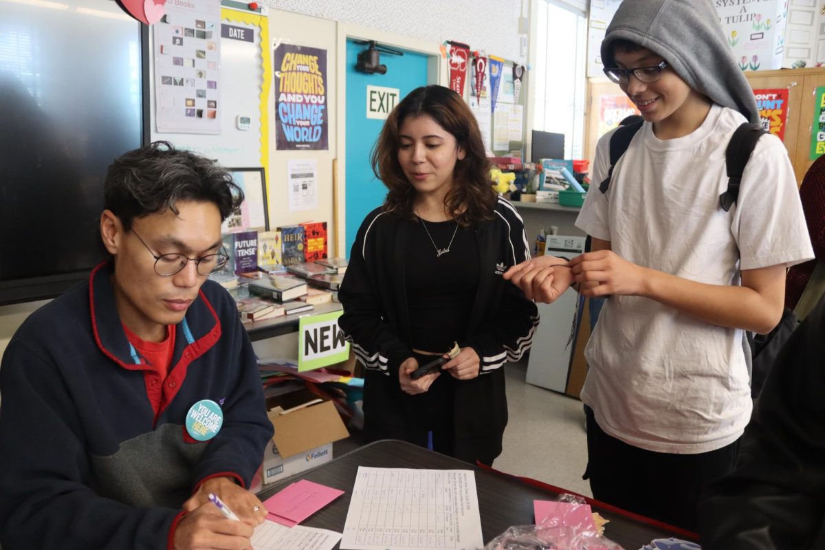 Librarian Alain Cruz sells Valentine's Day grams to junior Julia Garcia and freshman Jake Galdamez on Feb. 11. Valentine's Day grams were sold in the library during the weeks leading to Feb. 14 as a way to fundraise for school events.